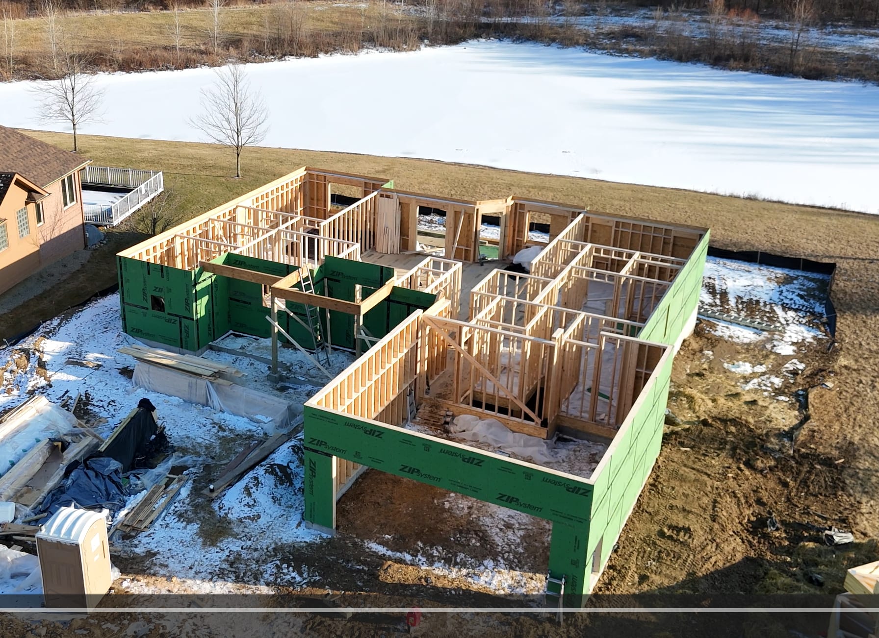 Aerial view of a new home framing project beside a pond in winter