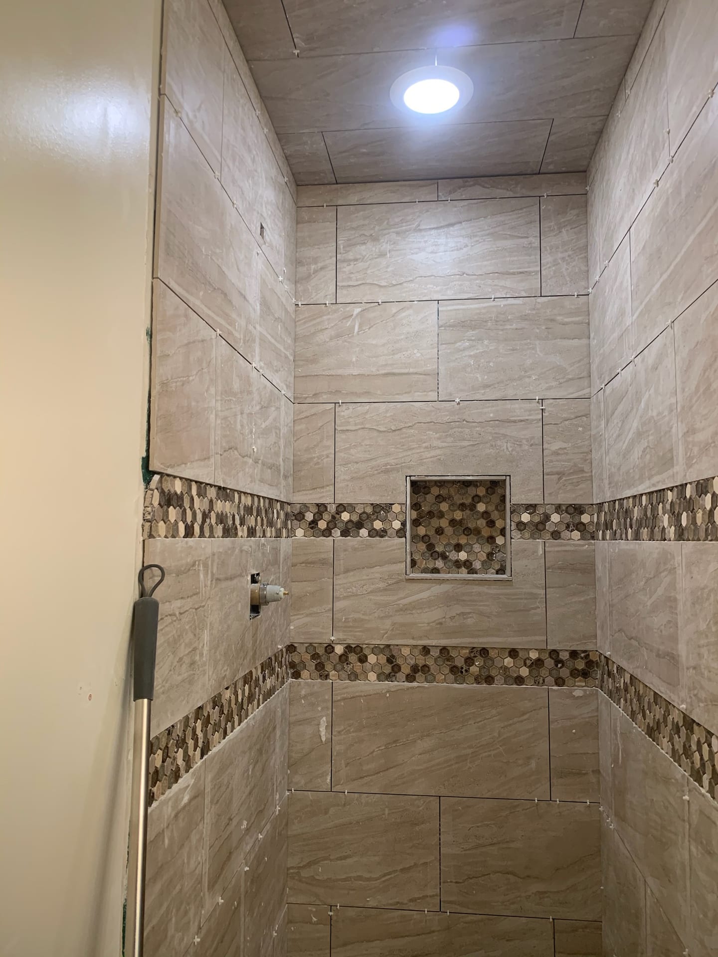 Walk-in shower with beige tile and copper-tone hex mosaic accent stripe